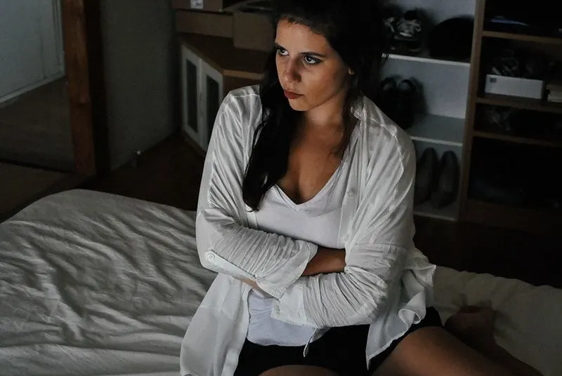 woman wearing white cardigan while sitting on the bed