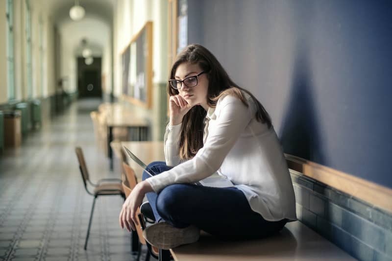 woman wearing white coat sitting on bench along the hallway