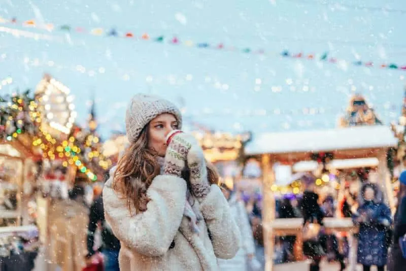 woman wearing winter outfit and drinking coffee at christmas market