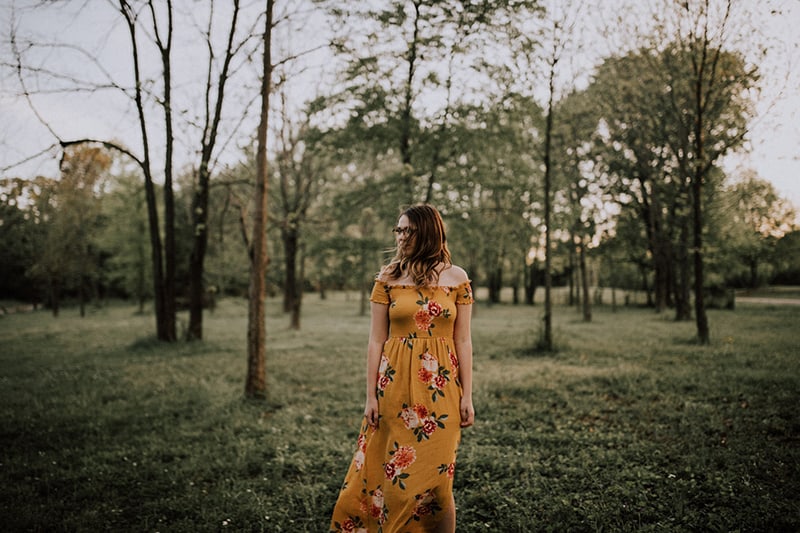 mulher com vestido floral amarelo a caminhar na floresta