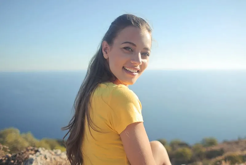 woman wearing yellow shirt sitting on the cliff