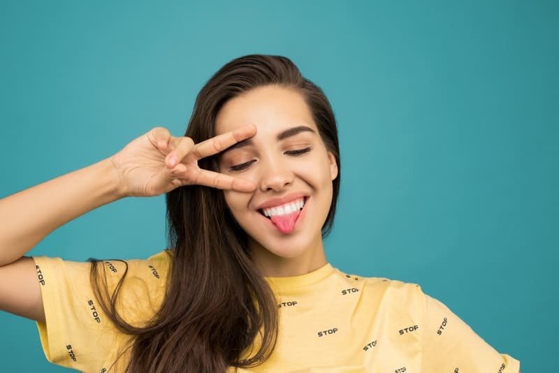 woman wearing yellow with hand sign and tongue out
