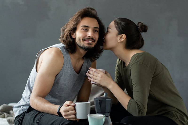 woman whispering a man in gray top while holding a cup