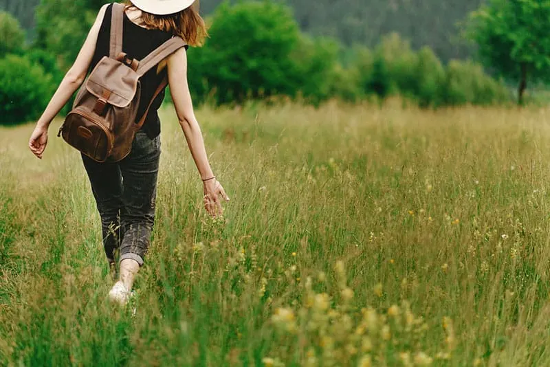 woman with backpack walking through grass