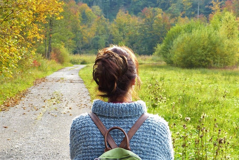 mujer con mochila que lleva suéter azul mientras camina en la naturaleza