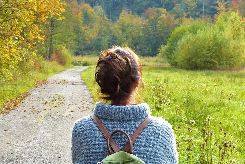 woman with backpack wearing blue sweater while walking in the nature