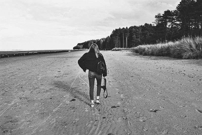 mujer con mochila caminando por la orilla del mar