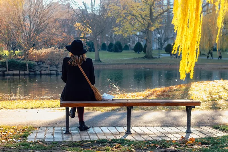 woman with black hat sitting on the bench beside the water