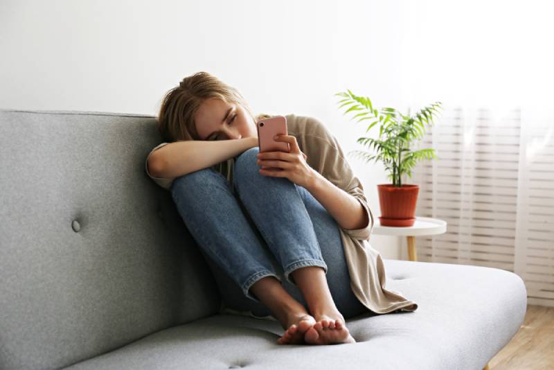 mujer con expresión facial deprimida sentada y sosteniendo su teléfono