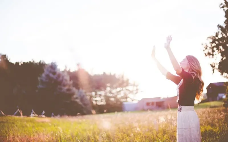 Woman with hands up standing on meadows during daytime