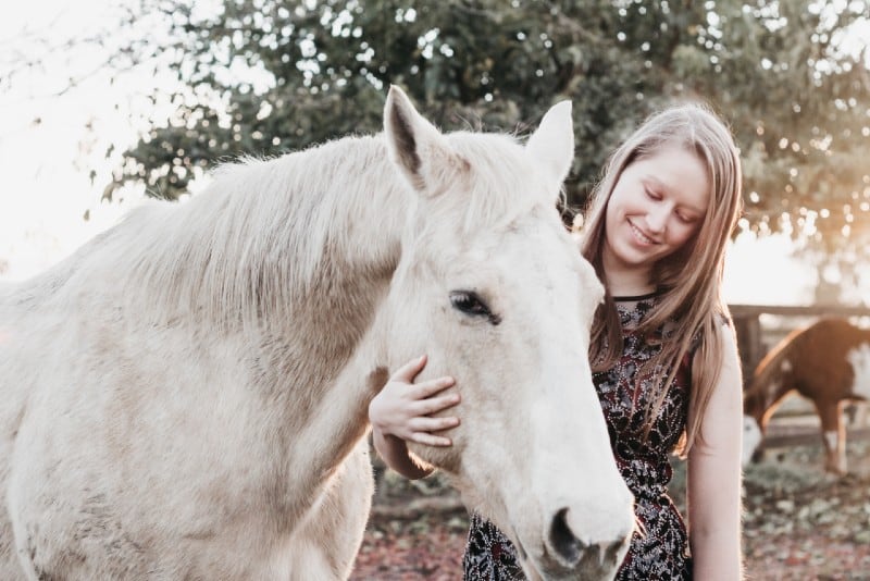 mulher sorridente a segurar um cavalo branco durante o dia