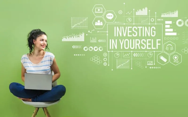 Happy woman sitting on a chair with laptop against green wall and invest in yourself message on it