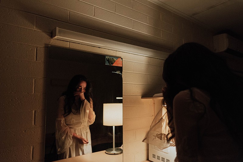 woman with long black hair crying in front of mirror