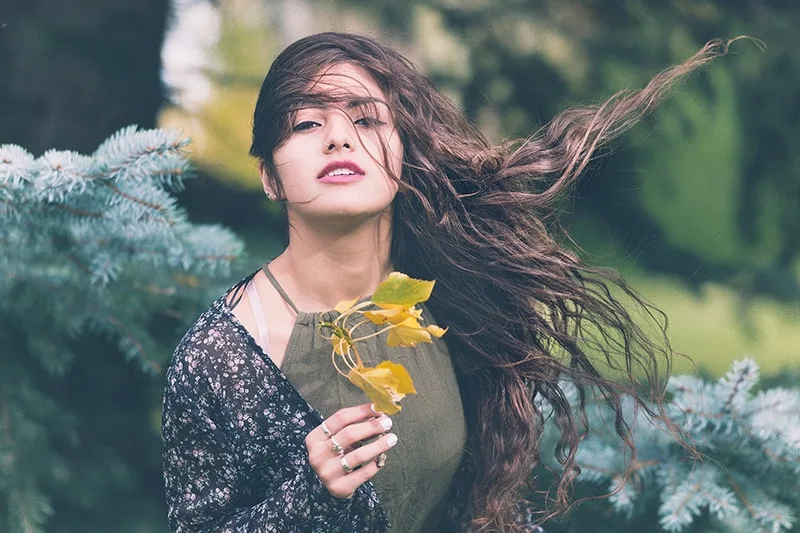 woman with long brown hair holding a branch with leaf