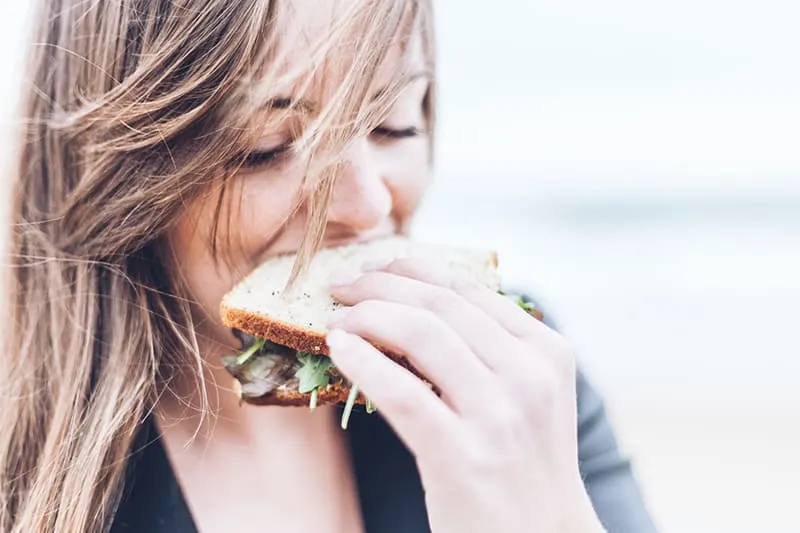 woman with long hair eating sandwich