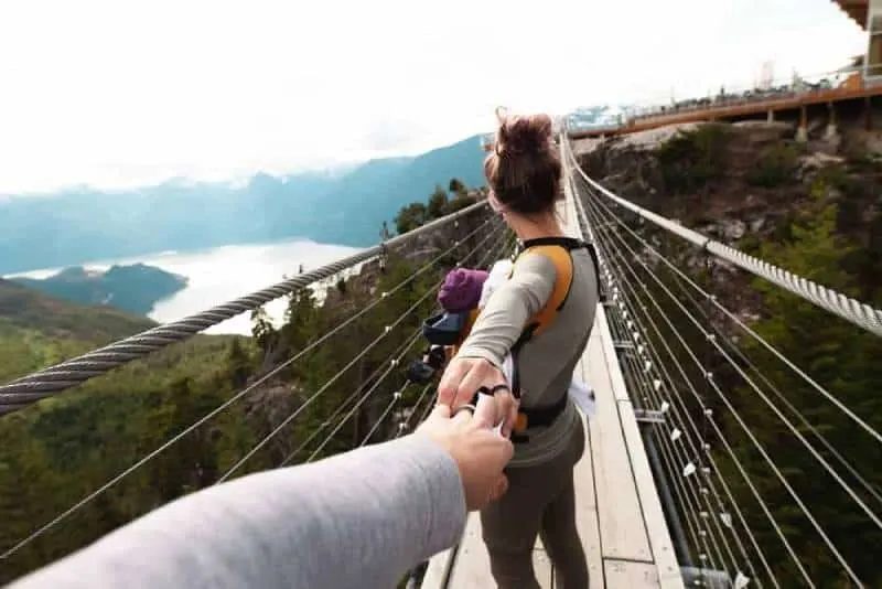 woman with yellow backpack standing on hanging bridge with trees