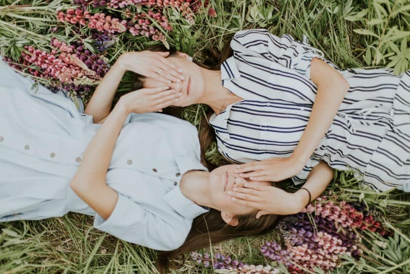 two women lying on grass and covering their eyes