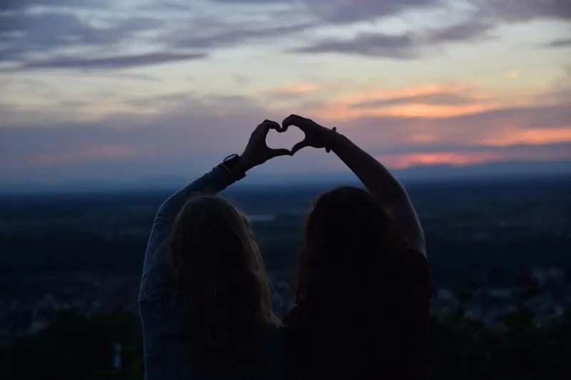 women forming heart gestures during sunset