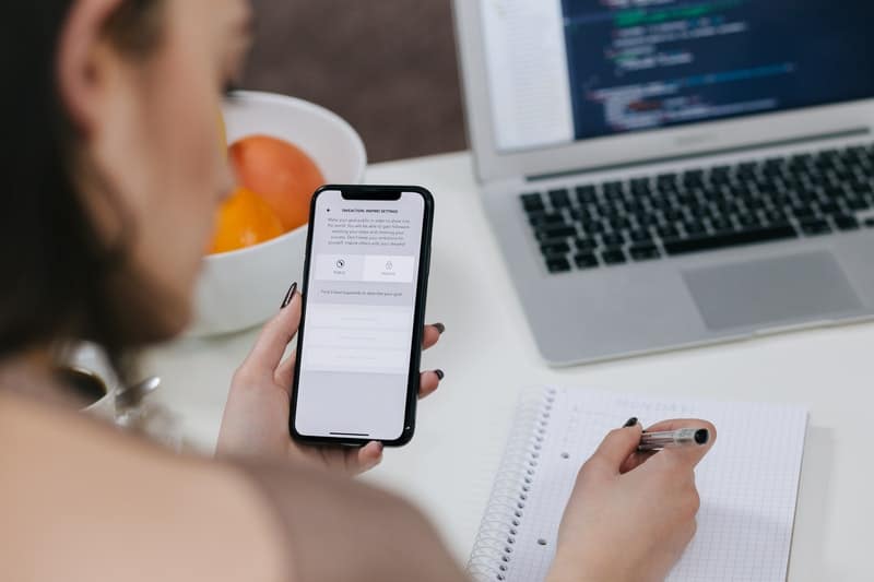 mujer sosteniendo iphone x gris espacial y escribiendo con boli sobre una mesa