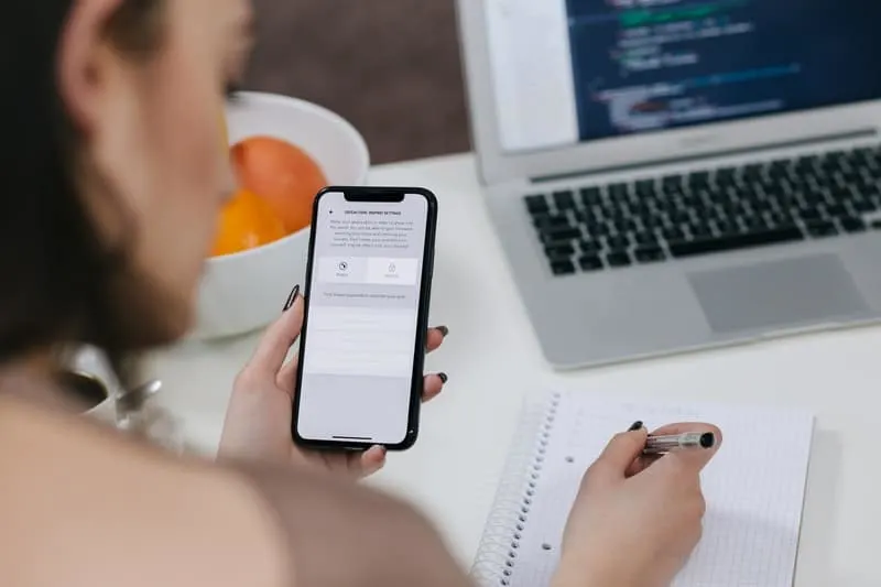 women holding space gray iphone x and writing using a pen on a table