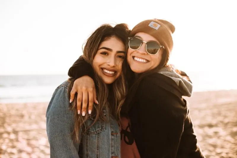 two women hugging and smiling on beach