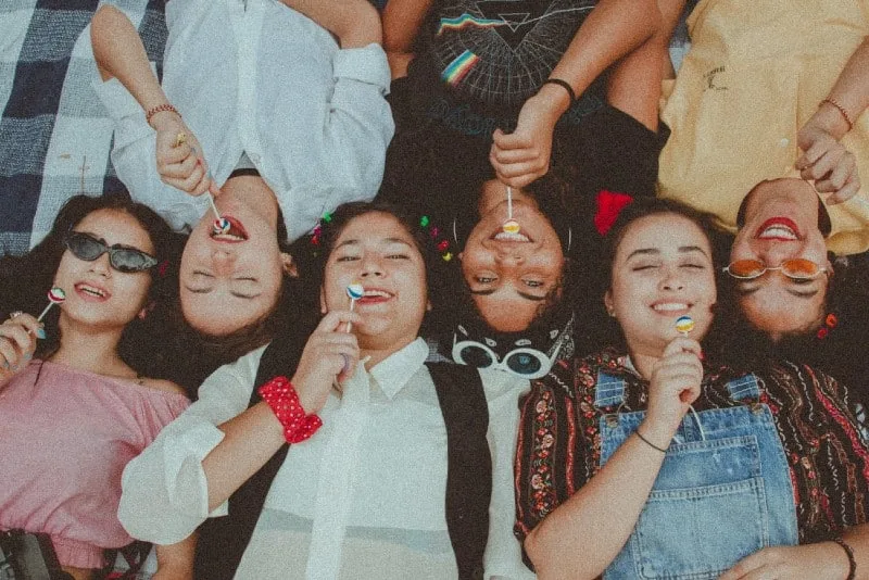 six women lying on blanket eating lollipop