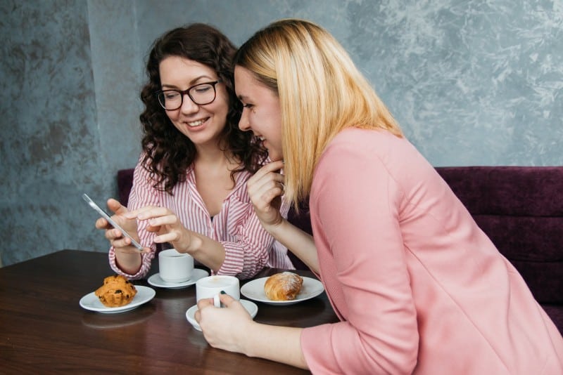 two women sitting at table looking at smartphone