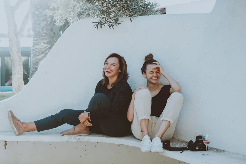 two women sitting on white bench and laughing