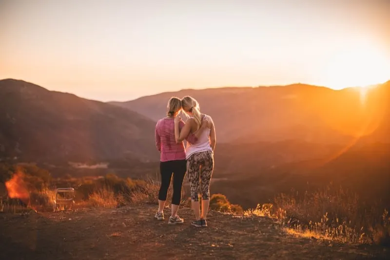 two women standing on mountain at sunset