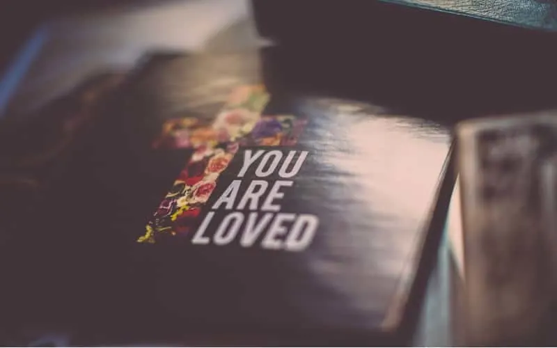 You are loved message written on a book cover near cross