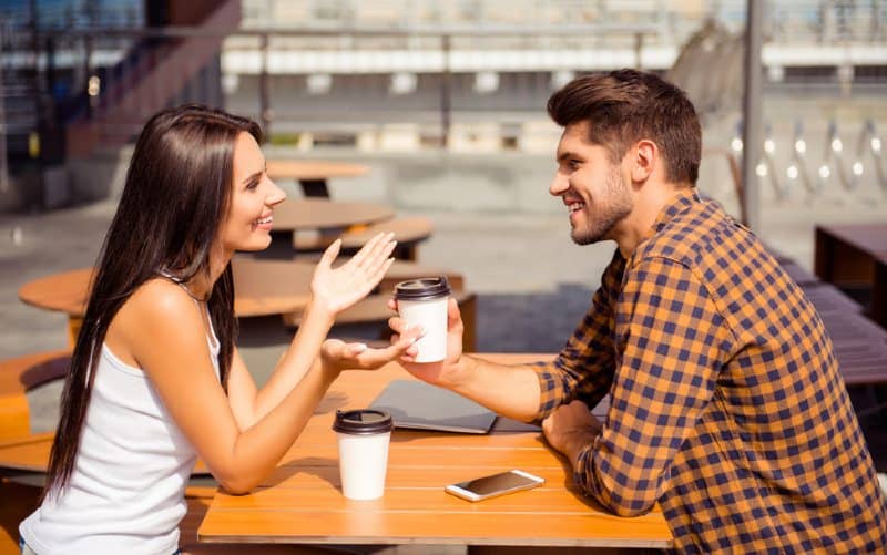 Giovane coppia felice seduta a un tavolo di fronte all'altra e che parla bevendo caffè