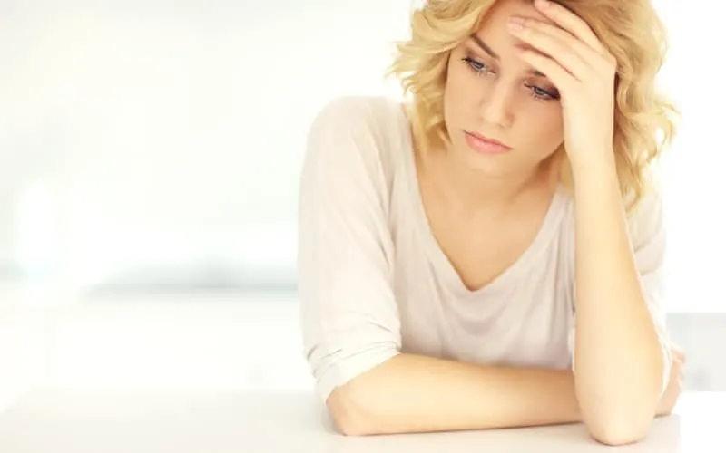 Young depressed blonde woman sitting with white background