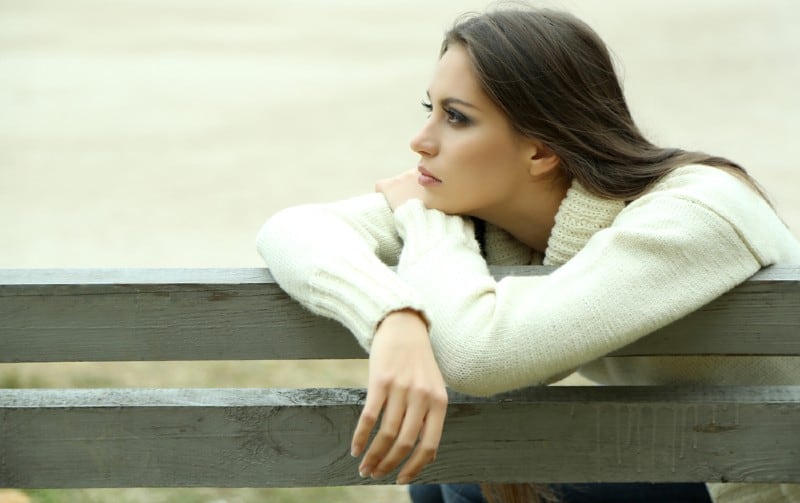 Mulher jovem e solitária sentada num banco durante o dia