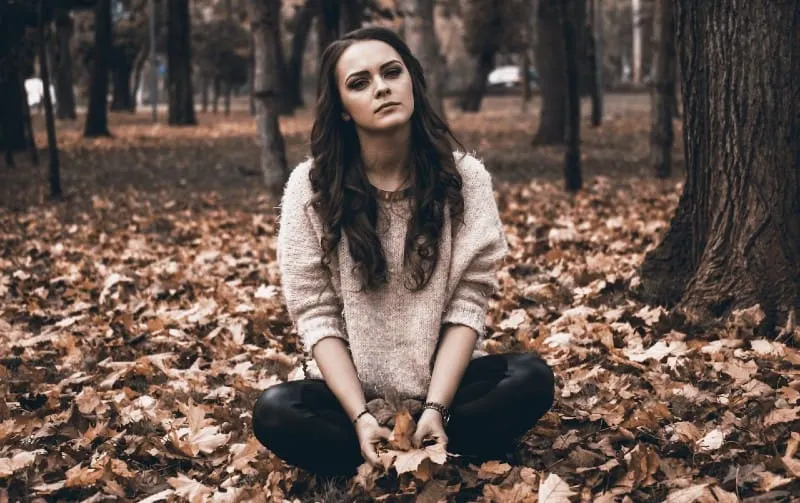 young woman siting on the ground in the forest in autumn time