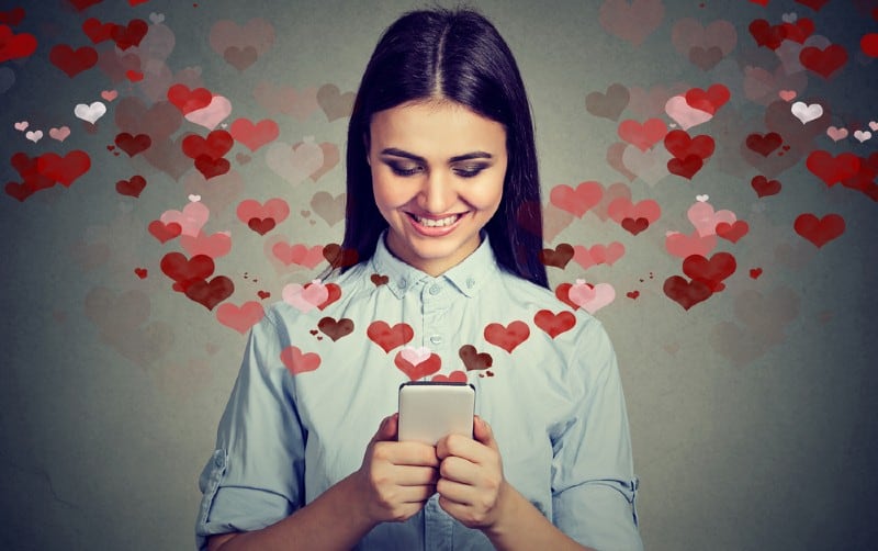 Giovane donna che manda un messaggio d'amore su smathphone con i cuori che volano intorno a lei