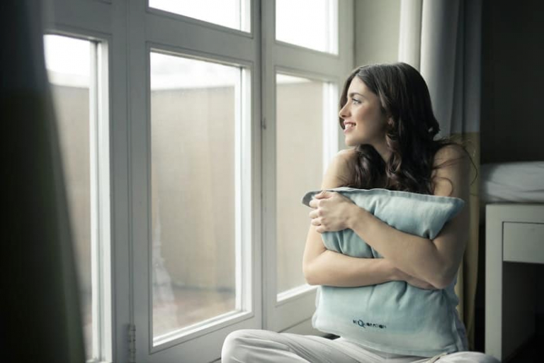 black-haired woman hugging gray pillow near glass panel window
