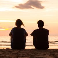 amici seduti insieme sulla spiaggia a guardare il tramonto