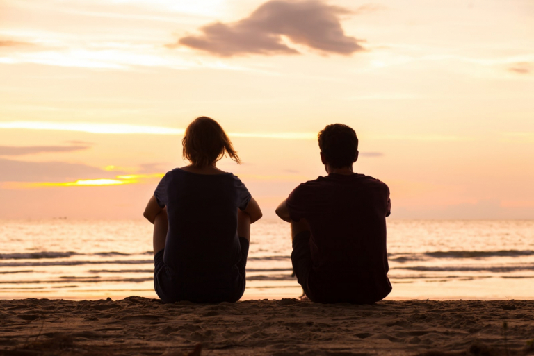 friends sitting together on the beach and watching sunset