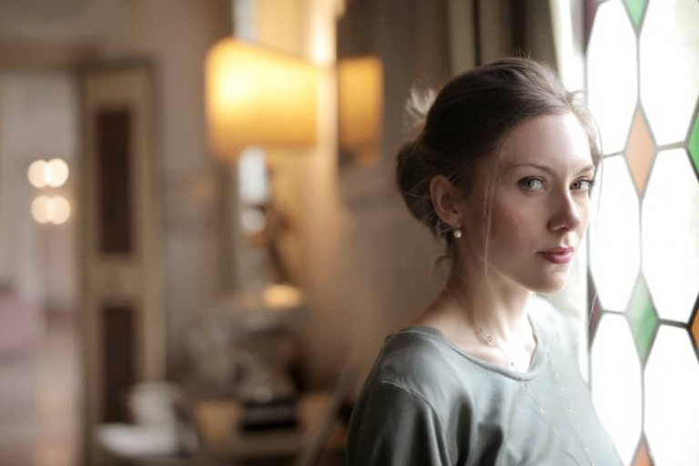 pensive woman in gray top standing near stained windows