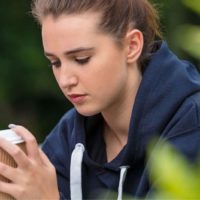 donna con capelli intrecciati e maglione blu che guarda triste mentre tiene in mano una tazza di caffè