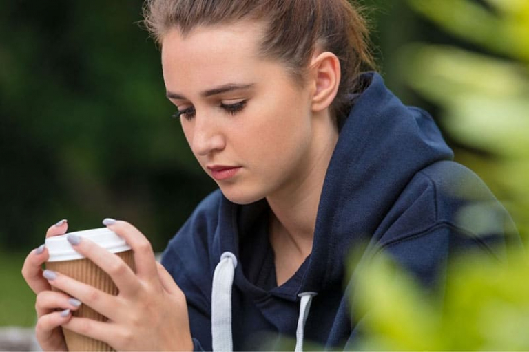 woman with braided hair and blue sweater looking sad while holding a cup of coffee