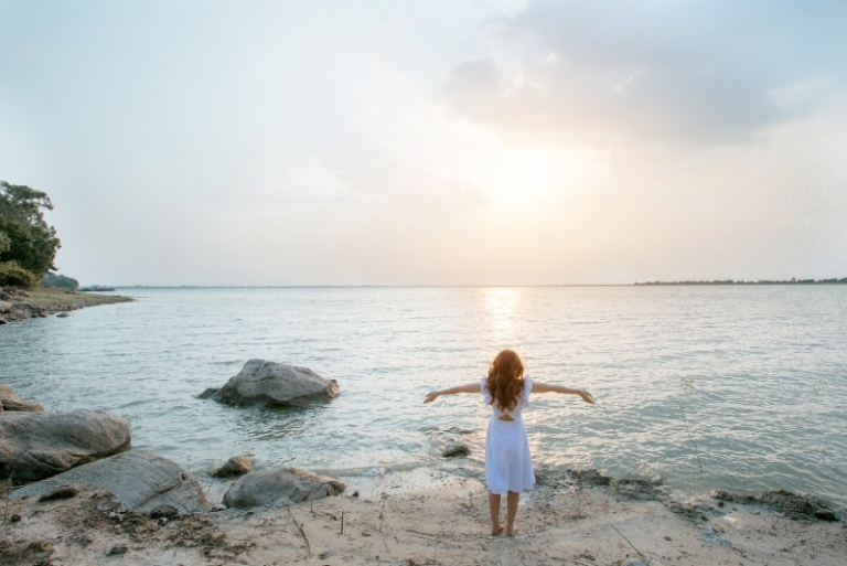 woman in white dress standing on rock looking at sea