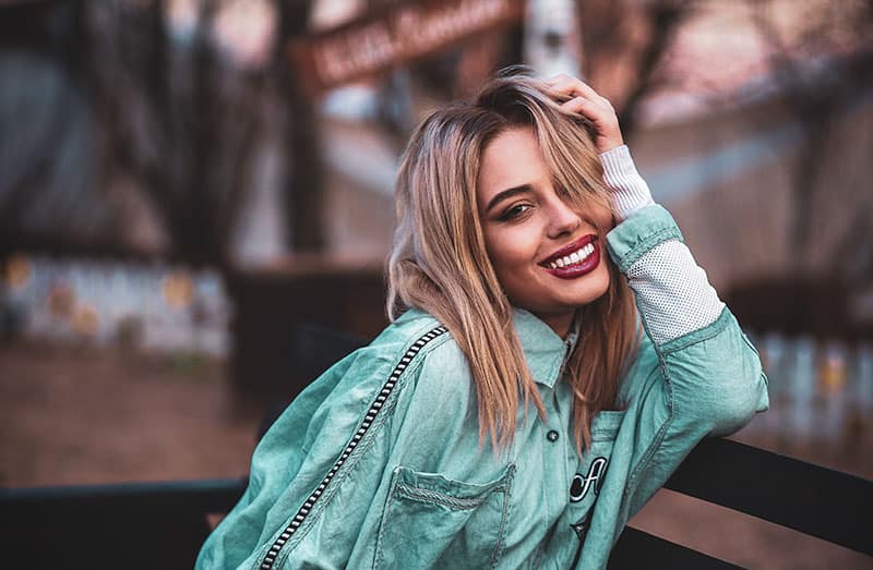 woman smiling while sitting and leaning on a table wearing teal jacket