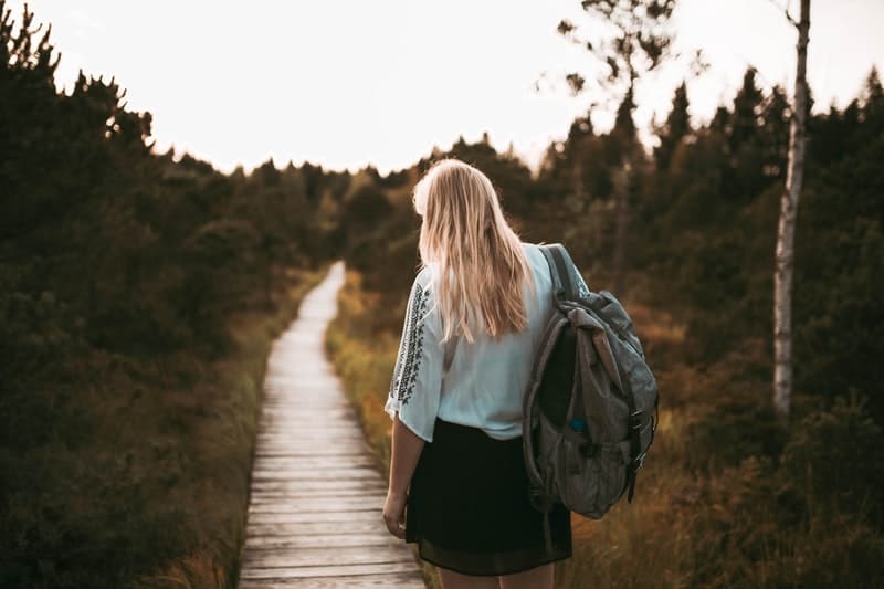 woman with a backpack walking on a wooden path in the middle of the grasses