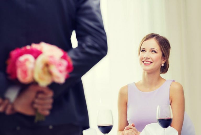 pretty woman sitting and a man carrying flowers hidden at his back
