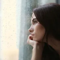 a sad black-haired woman looks out the window