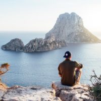 hombre con gorra sentado en una roca mirando al mar