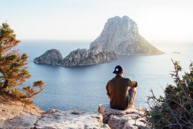 man with cap sitting on rock looking at sea