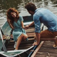 woman in a boat wearing blue dress assisted by a guy to get up by holding her hand