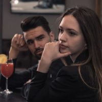 disappointed woman sitting beside a man in a bar with drinks on the table